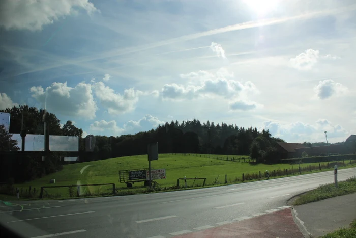 Eine Straße und grüne Felder unter einem blauen, leicht bewölkten Himmel.