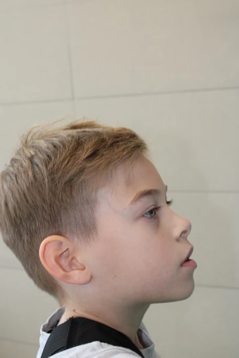 Das seitliche Porträt eines Jungen vor einer hellen Wand.