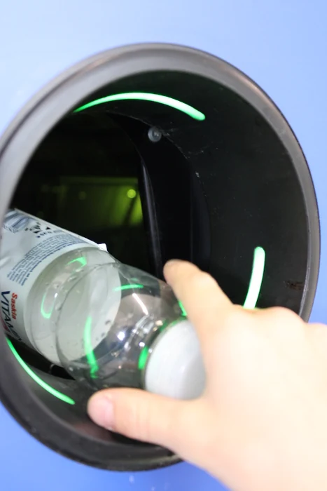 Eine Hand schiebt eine Plastikflasche in einen Pfandautomaten.