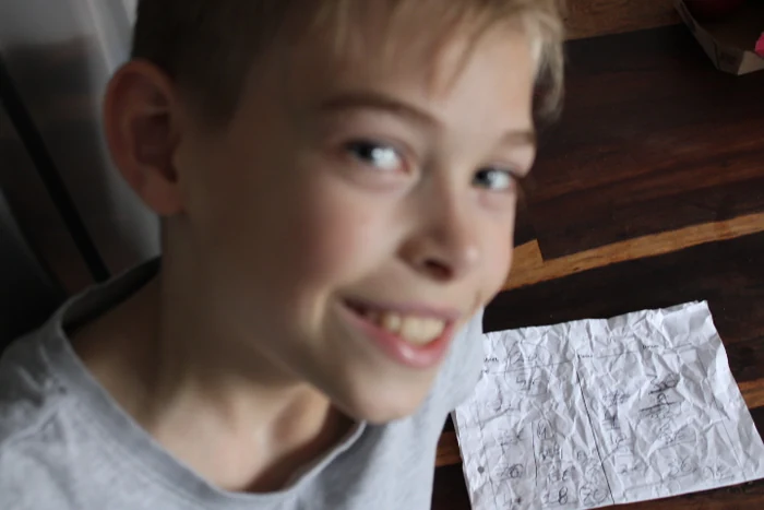 Ein lächelnder Junge neben einem Tisch mit einem beschriebenen Blatt Papier.