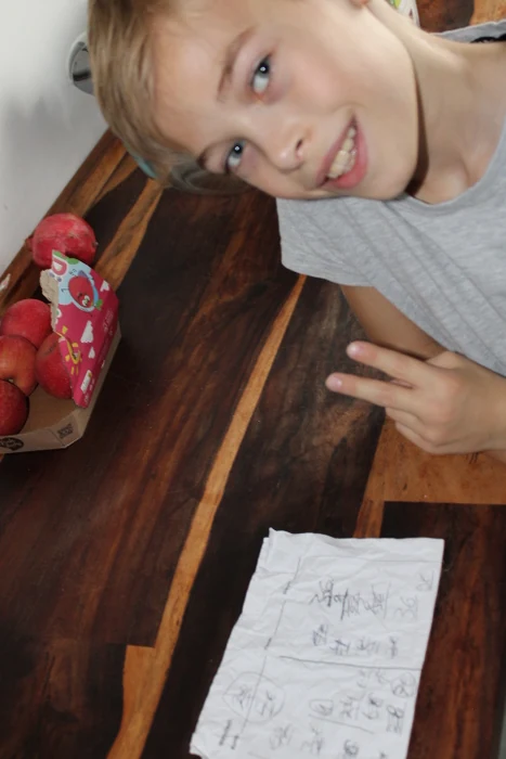 Ein Junge neben einem Holztisch mit Äpfeln und einem Blatt Papier.