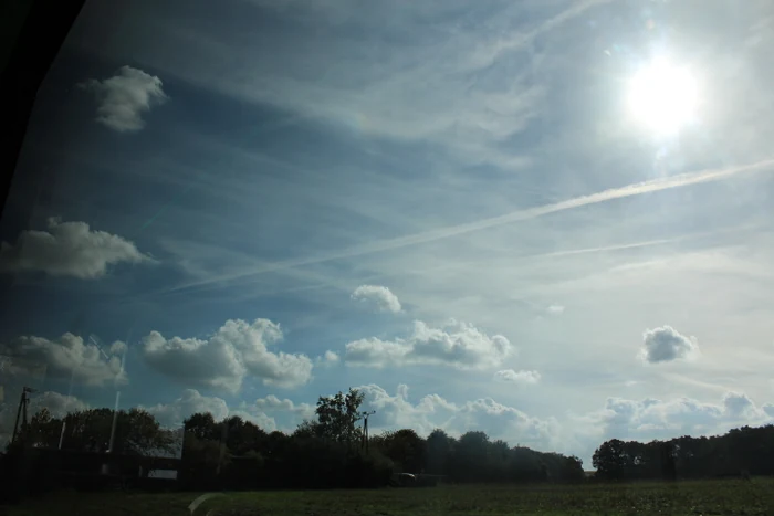 Sonnenstrahlen und kleine Wolken über einer grünen Landschaft.