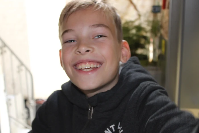Ein lächelnder Junge in einem dunklen Pullover.